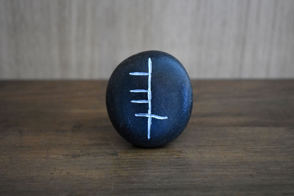 Ogham Ádh luck symbol on a smooth dark stone.