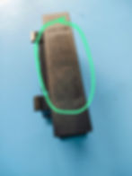 Injection-molded plastic part displaying a visible sink mark, highlighted in green. The defect appears as a slightly depressed or uneven surface, likely caused by uneven cooling or insufficient packing pressure during molding. The part is placed on a blue background, and the texture of the surface is rough with noticeable imperfections