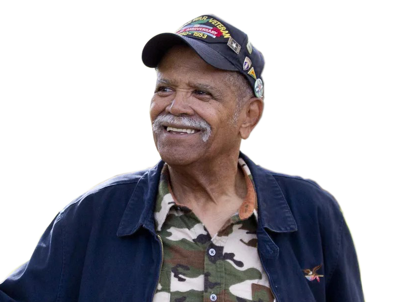 Louis Diggs, an older Black man wearing a cap and a camouflage-print shirt under an open jacket, smiling and looking off to the side.