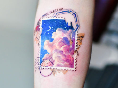 Collage-style tattoo of a dreamy sky with pink clouds and stars inside a vintage stamp border on a forearm