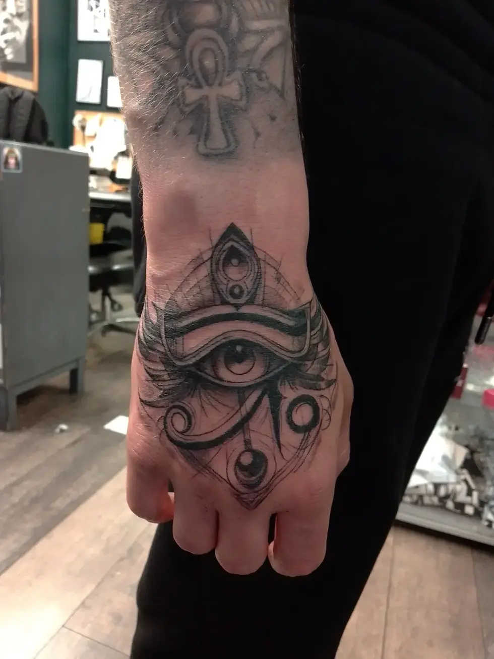 Close-up of a tattooed fist in a tattoo shop, showing a black eye motif on the back of the hand and forearm.