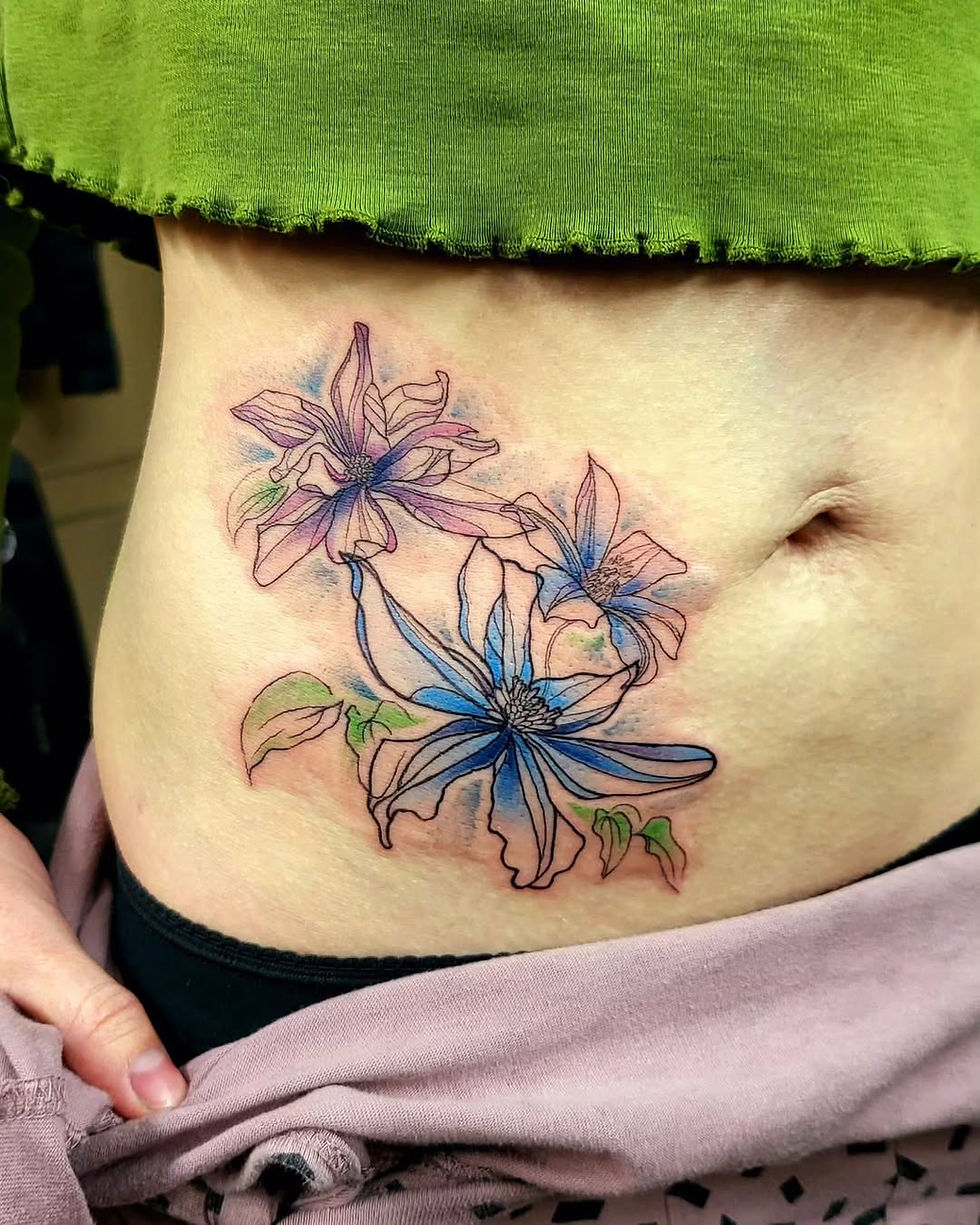 Close-up of a bare stomach with a pastel blue and pink floral tattoo, framed by a green top and pink pants.