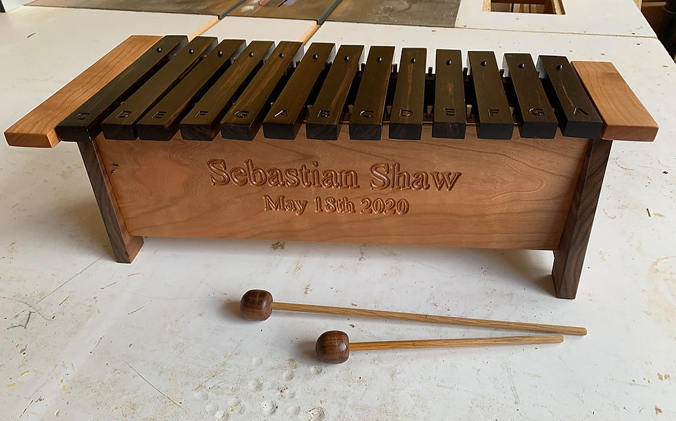 Wooden xylophone with dark keys labeled C to G on a light base. "Sebastian Shaw May 18th 2020" engraved. Two mallets on a white surface.