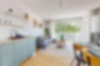 Salon cosy avec baie vitrée, cuisine épurée vert d’eau et coin repas en bois clair, dans une colocation à Genève, Lausanne, Nyon, Annemasse et Ferney-Voltaire.
