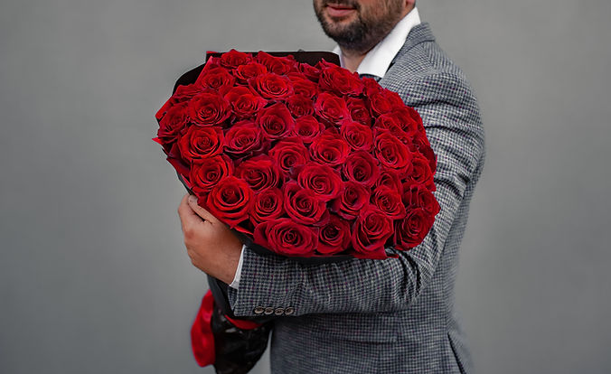 Young man in a suit holds a large bouquet of red roses on his shoulder, clenching his fist