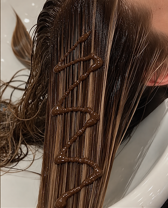 Wet brunette hair in white shampoo bowl that is slicked straight with brown professional hair color drizzled on the top