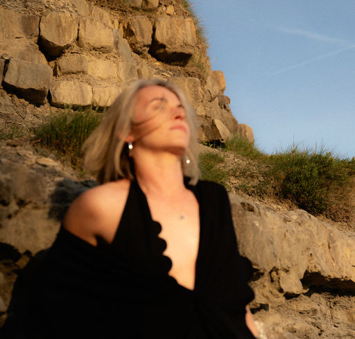 Woman confidently leaning back against the rocks with her eyes closed in the natural sunlight
