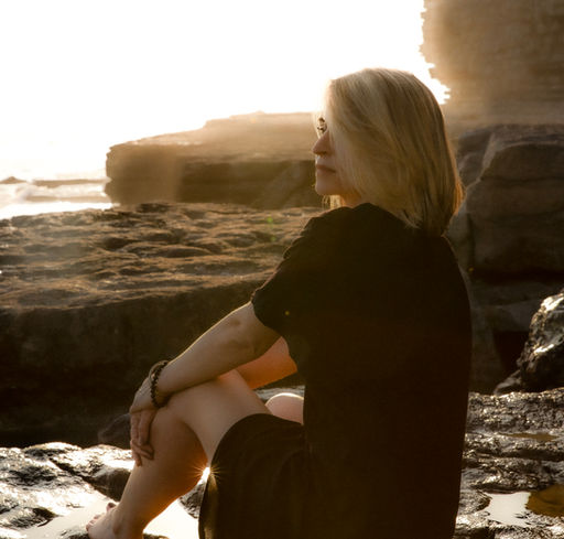 Side-profile silhouette of a woman sitting on the sand with the rocks in the background behind her.
