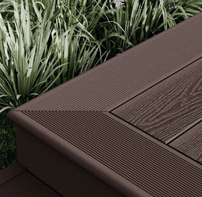 Dark wood composite decking showing edging, with some turf in shot