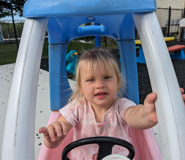 blonde haired toddler girl enjoying outdoor recreation in a ride on toy car at Building Futures, Streetsboro, Ohio