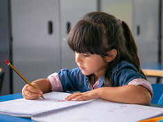 Menina em sala de aula escrevendo na folha sulfite com seu lápis.