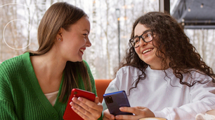 Duas amigas felizes com seus celulares por usarem cashback.