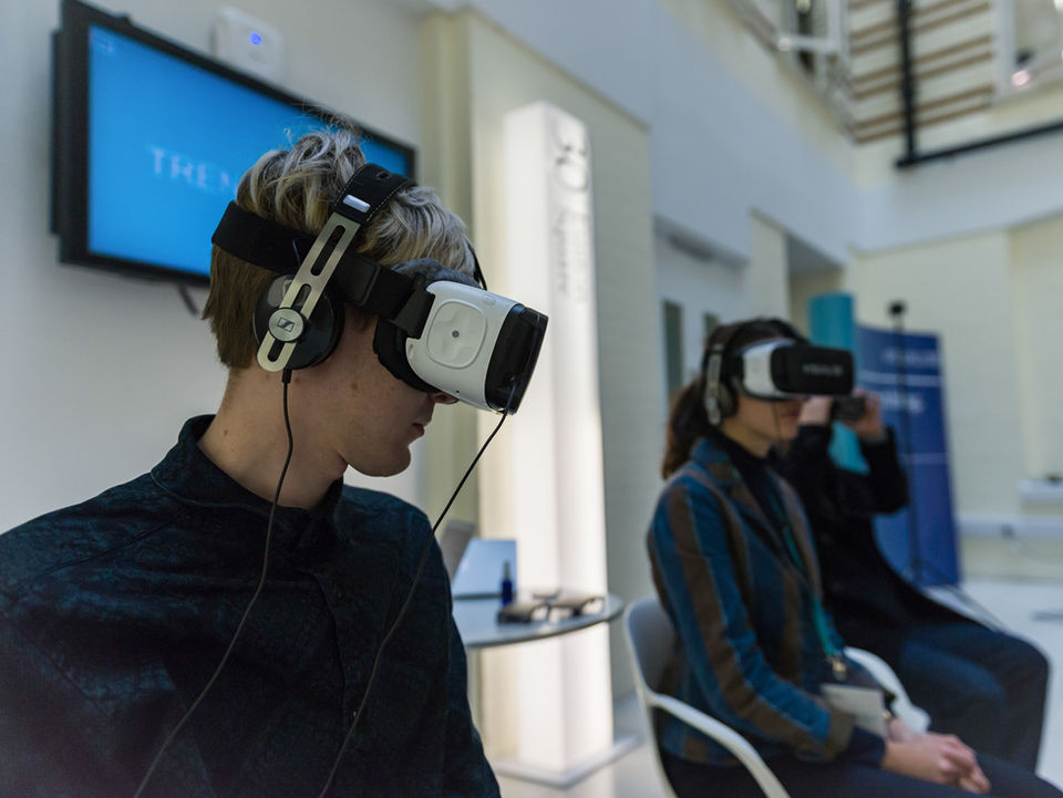 Photo of two people wearing VR headsets and sat watching a demo in the exhibition area at a business conference