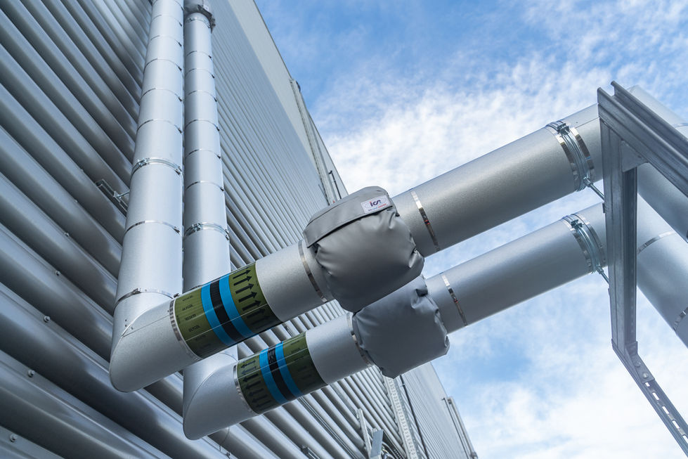 External insulated pipework fixed to warehouse facade against blue sky