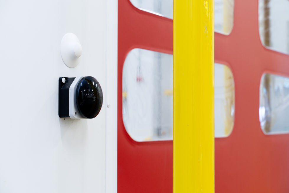 Sensor detail beside red rapid door and yellow safety bollard in temperature-controlled warehouse