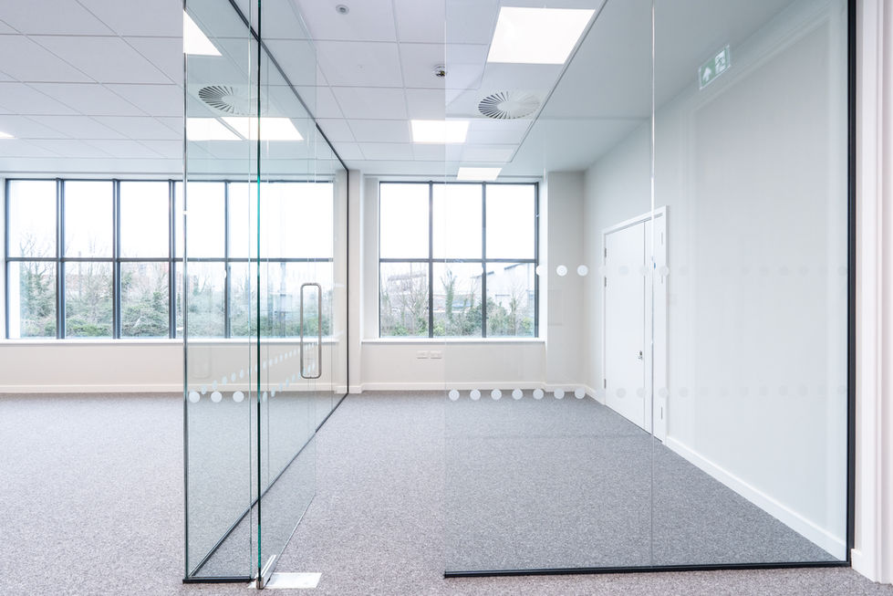 Small office kitchenette with white cabinetry, dark worktop and glazed partition wall
