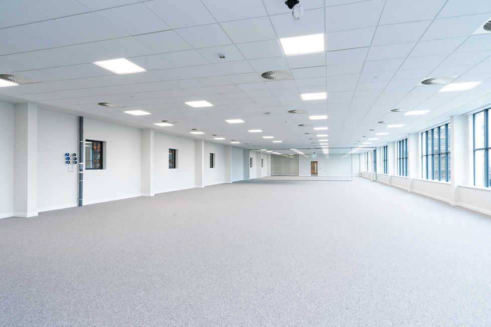 Glass-walled office room with carpet flooring and views across the wider office floor