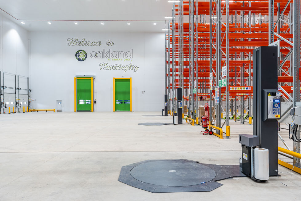Wide warehouse interior with branded wall, green doors and pallet racking