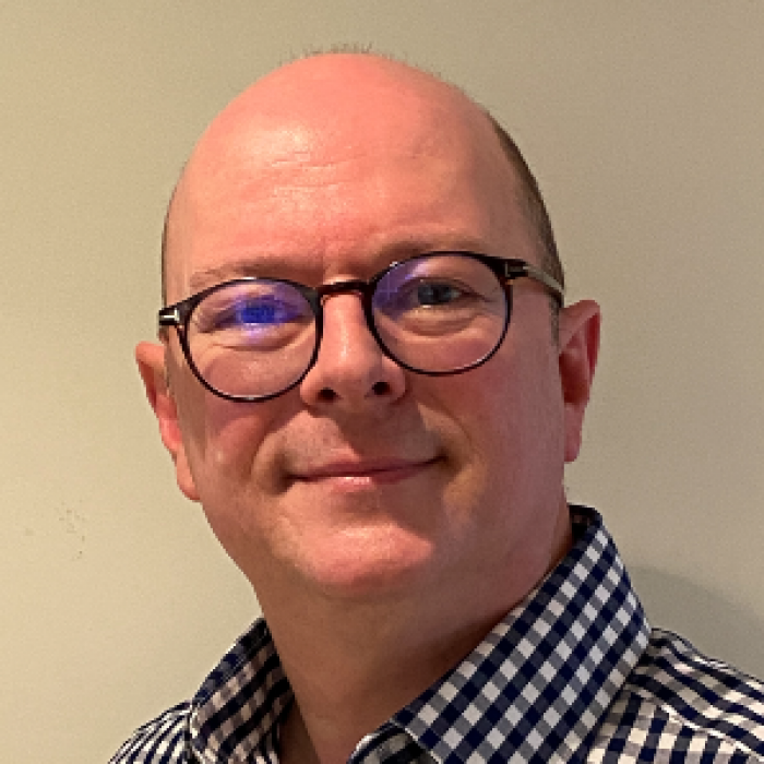 A headshot of a fair-skinned, bald man wearing glasses and smiling.
