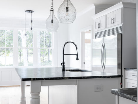 Contemporary kitchen with black lighting and plumbing fixtures, white cabinets, and granite countertops by general contractor near Morehead City, NC.
