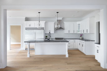 Modern white kitchen with leathered black countertops, black plumbing fixtures, black light fixtures, and white oak floors in a custom home by Coastline Signature Homes, leading builder in Beaufort, Emerald Isle, Atlantic Beach, and surrounding areas.
