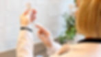 Person in white coat and gloves fills a syringe from a vial in a tiled room with plants. Focused and professional atmosphere.