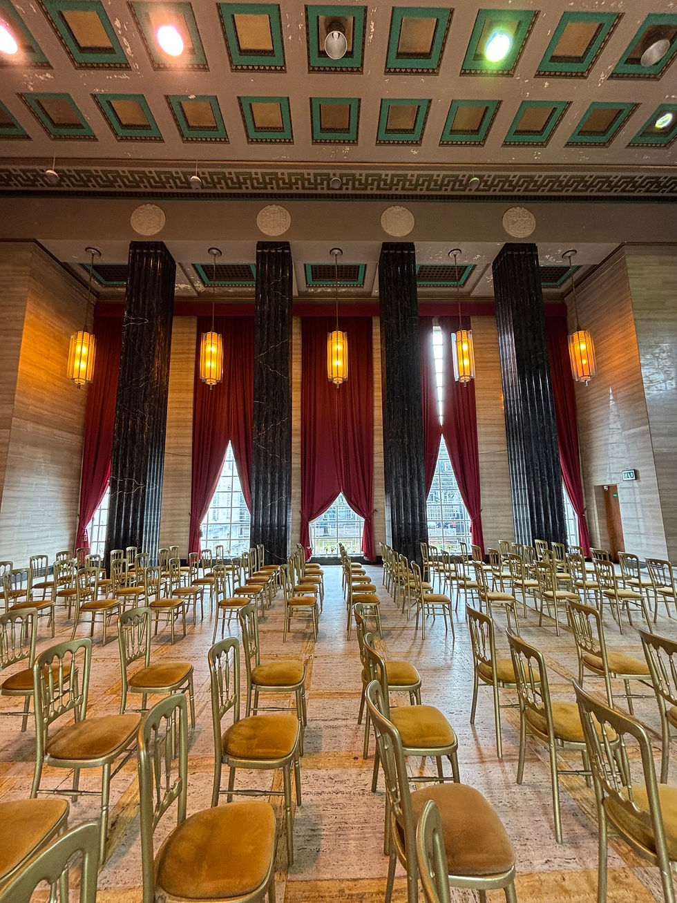 A grand hall with vintage golden chairs arranged in neat rows, surrounded by elegant columns and rich red drapery, setting a stately atmosphere beneath an ornate ceiling.