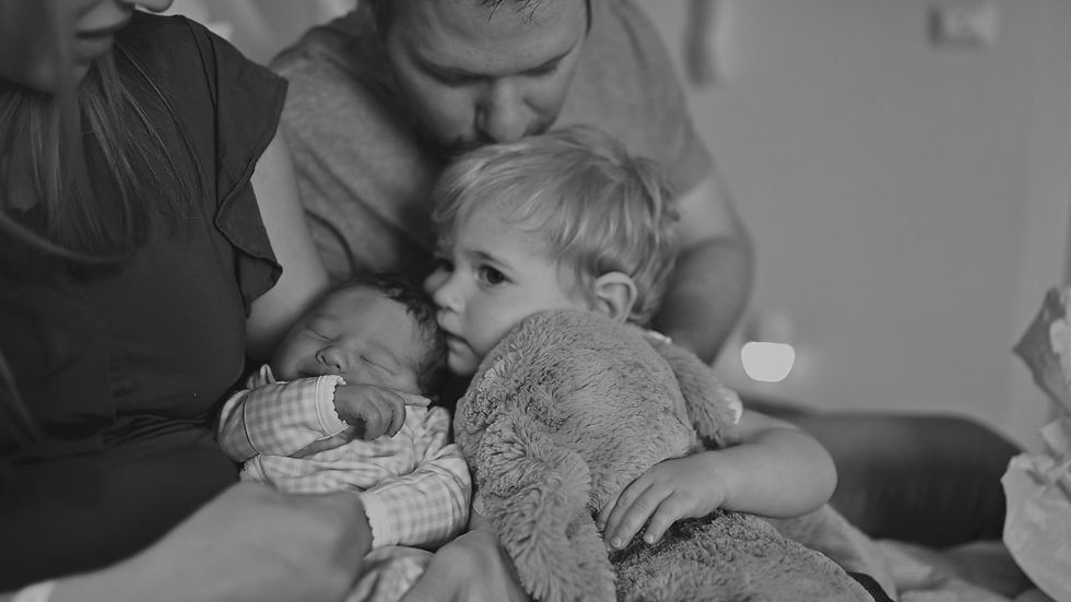 Older brother kissing his newborn sibling while holding his favorite stuffed animal