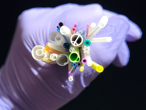 gloved hand holding a fistful of catheter medical tubing samples with the complex cross-sections on one end facing the viewer, representing catheter-based medical device coatings