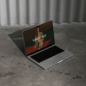 An open Macbook laptop sitting on a cement floor showing an aesthetic web design on the screen