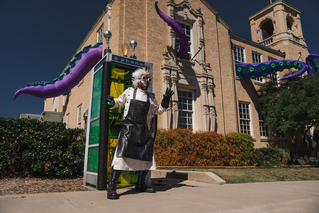 A person in a mad scientist costume standing in front of a building with tentacles coming out