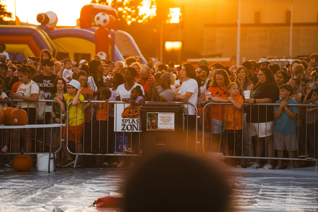 A crowd of people at sunset behind a barrier enjoying the Pumpkin Drop Event