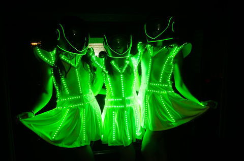 Three female astro LED guest greeters illuminted in a green light while wearing a head covering that looks like a helmet
