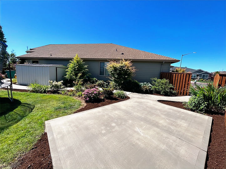 Concrete patio and landscaped backyard with garden beds.