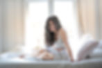 A woman sitting up in bed, hunched over with her hand on her stomach in pain