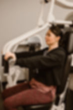 A photograph of a woman seated at an arm press/exercise equipment.