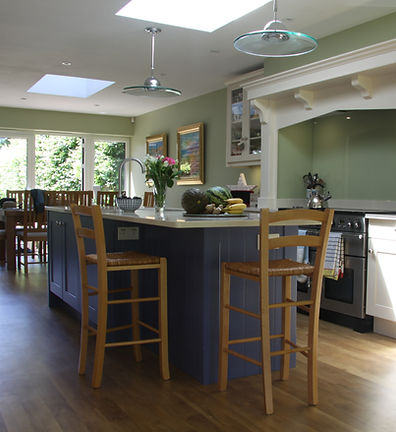 Sage green kitchen with a dark island, wooden bar stools and a painted mantel, The Highlands