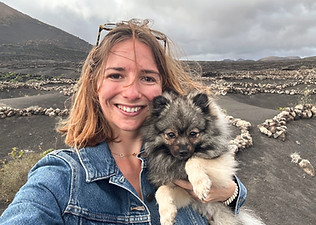 Emma Plantin smiling and holding her fluffy german spitz Loki in volcanic landscape – joy and wild connection.