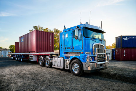 Kenworth prime mover with a container trailer parked in a transport yard. A Kenworth truck hauling a shipping container on a Midland trailer at a WATEX Transport depot. Kenworth prime mover coupled with a Midland container trailer at WATEX Transport, showcasing heavy vehicle capability and fleet presentation. A Kenworth prime mover with a Midland container trailer at the WATEX Transport yard, ready for container haulage operations. Container transport operations using a Kenworth truck and Midland trailer at WATEX Transport.