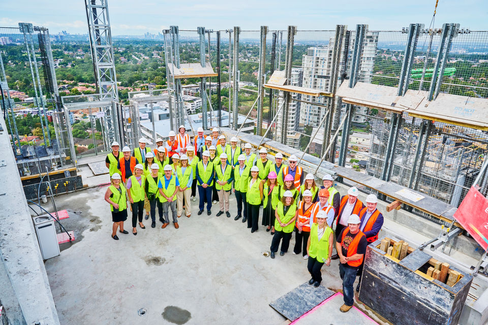 Construction team and project stakeholders gathered on a high-rise building site wearing hard hats and safety vests