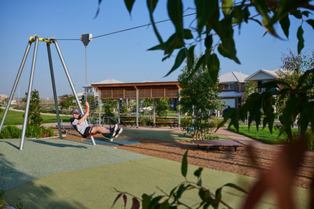 Child riding a zipline in a modern neighbourhood playground surrounded by landscaped green space, walking paths, and nearby homes, highlighting family-friendly park design, outdoor recreation, and community-focused living in a masterplanned residential area.