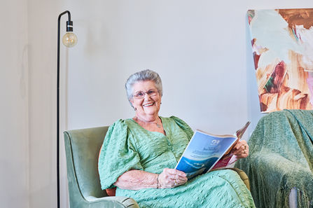 An older woman smiling while seated comfortably in an armchair, reading a magazine in a calm, well-lit living space.
A resident relaxing in a comfortable armchair, smiling while reading a magazine in a bright and welcoming aged care living area.A Carrington Care resident enjoying a quiet moment reading in a comfortable armchair, reflecting a warm, supportive aged care environment.
An older resident smiling as she reads in a cosy armchair within a light-filled Carrington Care living space, highlighting comfort, dignity, and quality of life.
A relaxed resident reading in a comfortable aged care living space.