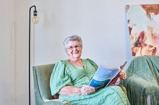 An older woman smiling while seated comfortably in an armchair, reading a magazine in a calm, well-lit living space.
A resident relaxing in a comfortable armchair, smiling while reading a magazine in a bright and welcoming aged care living area.A Carrington Care resident enjoying a quiet moment reading in a comfortable armchair, reflecting a warm, supportive aged care environment.
An older resident smiling as she reads in a cosy armchair within a light-filled Carrington Care living space, highlighting comfort, dignity, and quality of life.
A relaxed resident reading in a comfortable aged care living space.