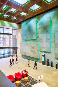 Interior of a modern office lobby with people walking through a large open space and illuminated architectural walls.
Spacious modern building lobby with people walking through an open atrium, featuring green illuminated wall details, high ceilings, and contemporary seating.
A large contemporary lobby interior with a high patterned ceiling, green illuminated feature walls, and people moving through the space, with red lounge chairs in the foreground.
Contemporary lobby interior with dramatic lighting, geometric ceiling details, and an open public space.