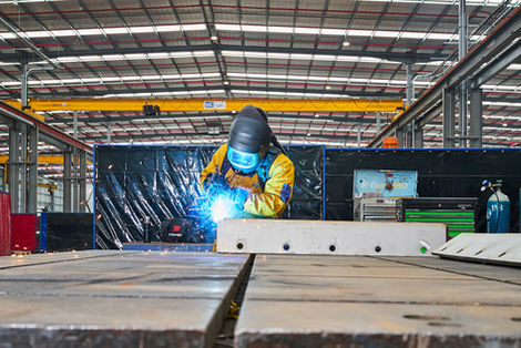 Welder wearing protective gear welding a metal component inside a factory. A welder in protective equipment welding a steel component on the factory floor, with sparks visible. Skilled welder carrying out metal fabrication work in an industrial workshop, with sparks flying during the welding process. A welder in full protective gear welding a steel component inside a large industrial workshop, capturing precision, safety, and craftsmanship in manufacturing. Metal fabrication in progress as a welder joins steel components inside an industrial facility.