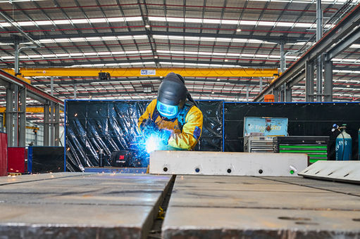 Welder wearing protective gear welding a metal component inside a factory. A welder in protective equipment welding a steel component on the factory floor, with sparks visible. Skilled welder carrying out metal fabrication work in an industrial workshop, with sparks flying during the welding process. A welder in full protective gear welding a steel component inside a large industrial workshop, capturing precision, safety, and craftsmanship in manufacturing. Metal fabrication in progress as a welder joins steel components inside an industrial facility.