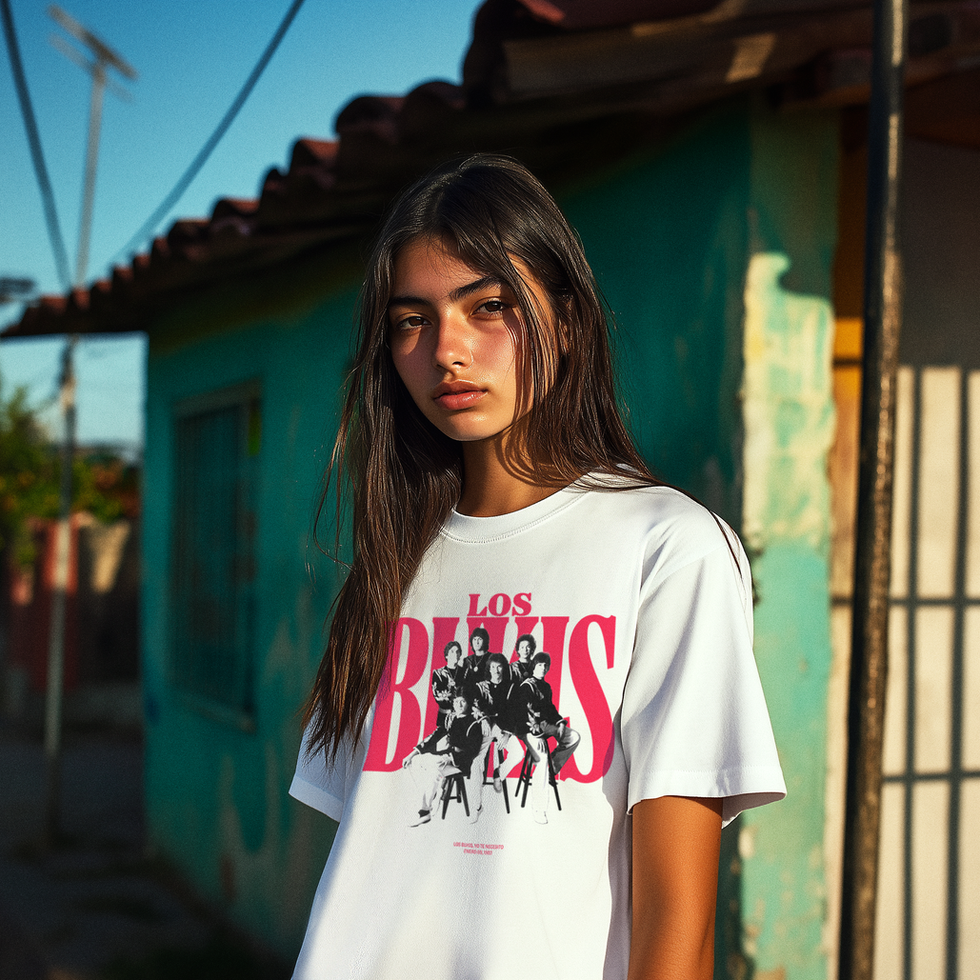 Young man wearing white Los Bukis band T-shirt with red logo, standing in turquoise alley with yellow door