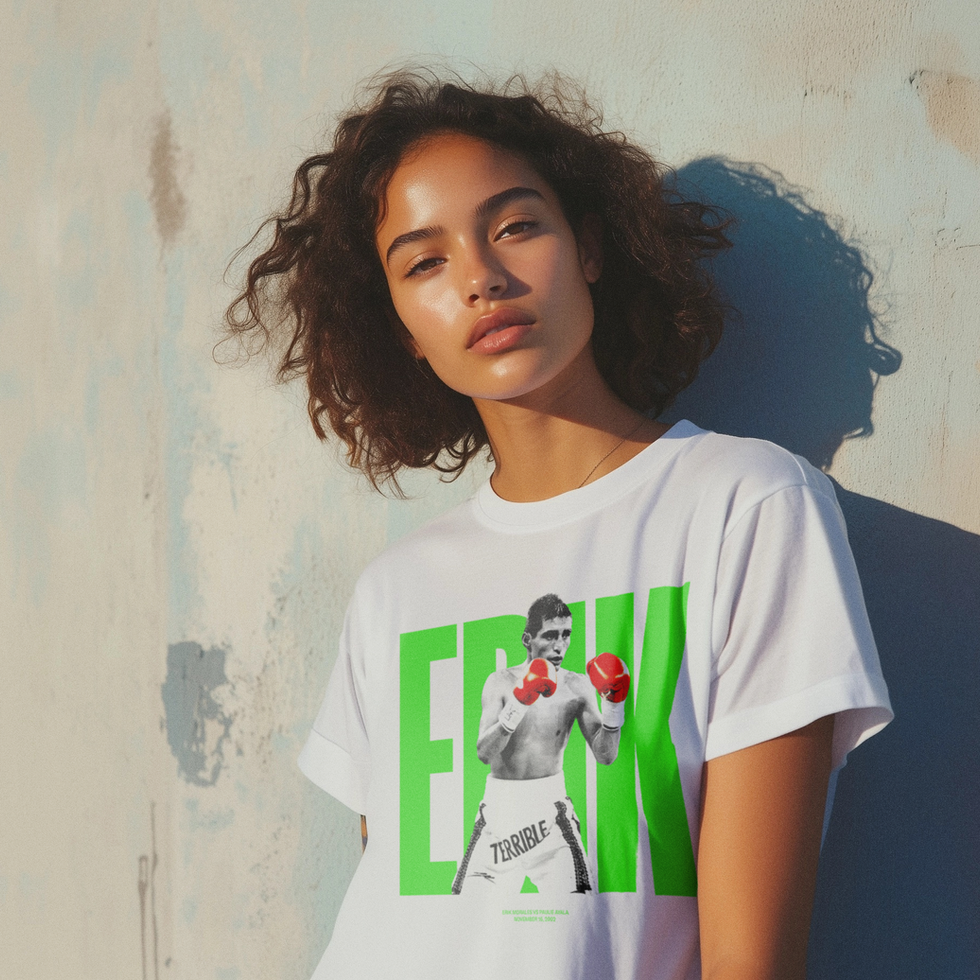 A woman with curly hair wearing a white Erik Morales T-shirt featuring “El Terrible” in green bold letters and red gloves