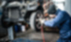 Mechanic in blue uniform using an air wrench on a car wheel at a garage