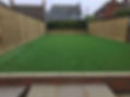 A neatly landscaped backyard with artificial grass and new wooden fences